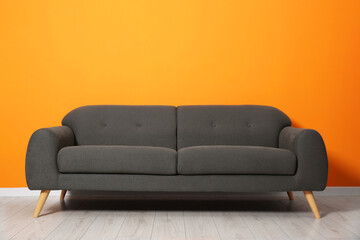 One stylish grey sofa near orange wall