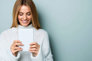 Fototapeta premium Smiling woman in cozy sweater using tablet against light background