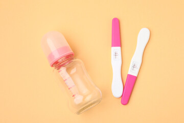 Pregnancy tests and baby bottle on pale orange background, top view