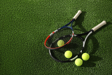 Tennis rackets and balls on green artificial grass, flat lay. Space for text