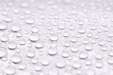 Water drops on light gray background, closeup view