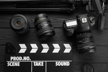 Movie clapper, camera and lens on black wooden table, flat lay