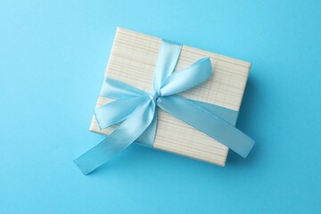 Gift box with bow on light blue background, top view