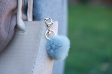 Woman with faux fur keychain on her bag outdoors, closeup. Selective focus