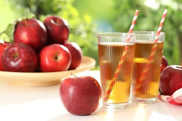 Tasty apple juice in glasses and fresh fruits on white table outdoors