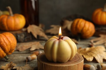 Autumn atmosphere. Burning pumpkin shaped candle and dry leaves on wooden table, closeup