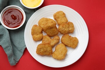 Delicious chicken nuggets and sauces on red background, flat lay