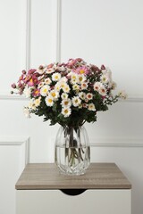 Vase with beautiful flowers on wooden nightstand near white wall