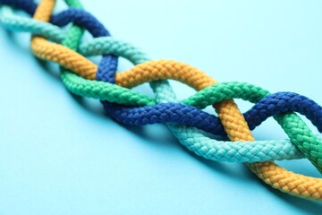 Braided colorful ropes on light blue background, closeup. Unity concept