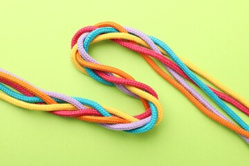 Braided colorful ropes on light green background, top view. Unity concept