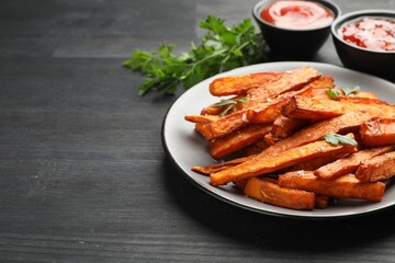Delicious sweet potato fries with spices and sauces on black wooden table, closeup. Space for text
