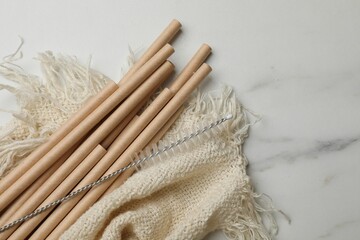 Bamboo drinking straws and cleaning brush on marble table, top view