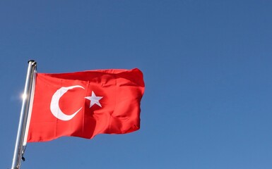 The Turkish flag waves proudly in the sky, displaying its striking red background. At the center, a...