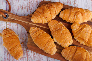 Top view of croissants on a wooden cutting board over a light wood table, showcasing the crisp and golden texture of the baked goods in a simple setting