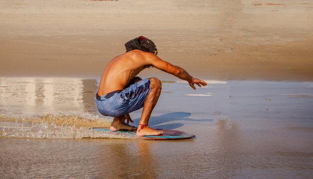 An unidentifiable skimboarder with a shirt over his head skimboarding on a beach. 