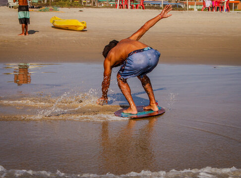 An unidentifiable skimboarder with a shirt over his head skimboarding on a beach. 