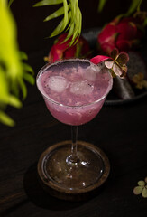 Refreshing dragon fruit cocktail garnished with ice and flower on dark wooden table