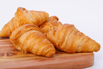 Golden croissants on a wooden cutting board placed against an infinite white background, showing texture and detail in the pastry's layers