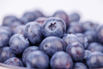 Detailed close-up of a ceramic pot filled with fresh blueberries on a white seamless background