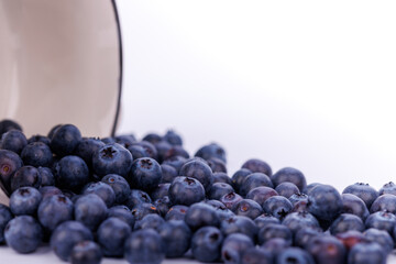 A stunning close-up of fresh blueberries cascading from an overturned bowl onto a seamless white background, showcasing the beauty of the fruit