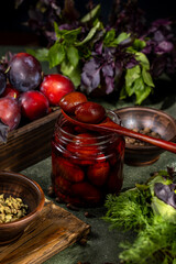 Pickled plums preserved in glass jar with fresh herbs and spices