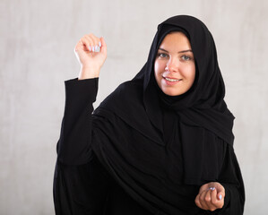 positive young woman in black hijab is actively gesticulating with her hands, opened palms and...