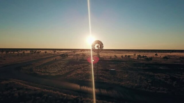 Aerial view. Silhouette of a large windmill in central Australia rotating in slow motion against dramatic Australian outback sunset. No people. Red center Uluru
