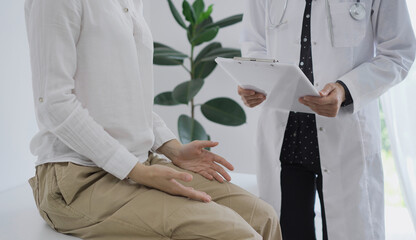 Obraz premium Doctor and a patient. The female physician, wearing a white medical coat standing with a clipboard during a consultation in the clinic. Medicine concept