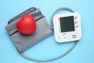 Blood pressure measuring device and squeeze heart on light blue background, top view