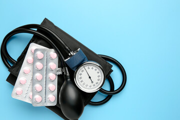 Blood pressure measuring device and pills on light blue background, top view