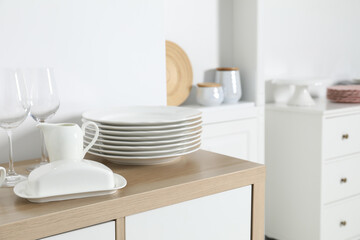 Tableware on wooden storage cabinet near white wall indoors