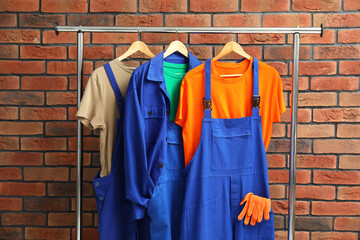 Different workers' uniforms on clothing rack near brick wall