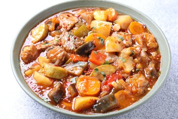 Delicious stew with vegetables in bowl on light grey table, closeup