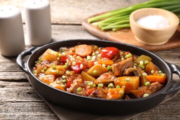 Delicious stew with vegetables in baking dish and spices on wooden table, closeup