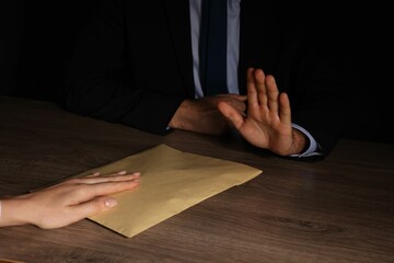 Corruption concept. Woman giving envelope with money to man at wooden table, closeup