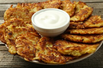 Delicious potato pancakes and sour cream on wooden table, closeup