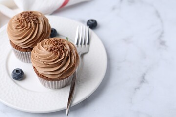 Tasty cupcakes with chocolate cream and blueberries on white marble table, space for text