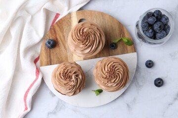 Tasty cupcakes with chocolate cream and blueberries on white marble table, flat lay