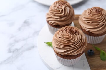 Tasty cupcakes with chocolate cream on white marble table, closeup. Space for text