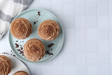 Tasty cupcakes with chocolate cream on white tiled table, flat lay. Space for text