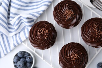 Tasty cupcakes with chocolate cream and blueberries on white tiled table, flat lay