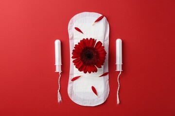 Menstrual pad with flower and tampons on red background, flat lay