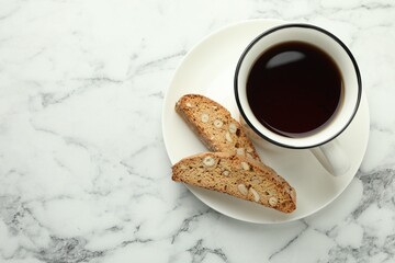 Traditional Italian almond biscuits (Cantucci) and cup of coffee on white marble table, top view. Space for text