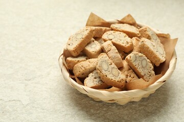 Traditional Italian almond biscuits (Cantucci) in wicker bowl on light textured table, closeup