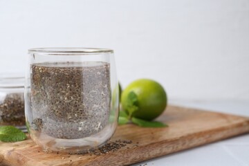 Glass of drink with chia seeds and lime on white table, space for text