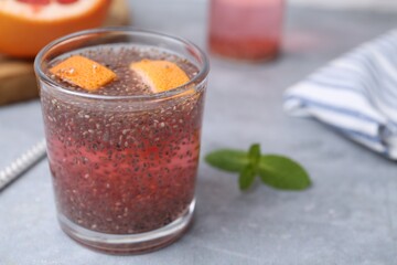 Glass of drink with chia seeds and grapefruit on grey table, closeup