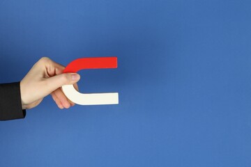 Woman with horseshoe magnet on blue background, closeup. Space for text