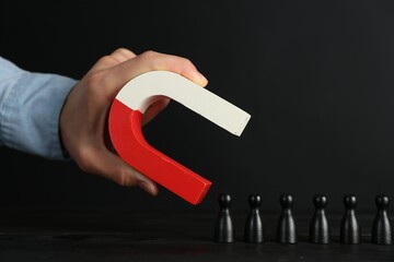 Man with magnet attracting black pieces at wooden table, closeup