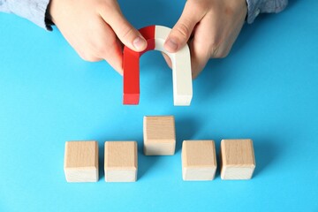 Man with magnet attracting wooden cubes on light blue background, closeup