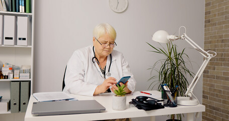 Mobile phone device in female doctor hands in office. Woman doctor using technology during break time.